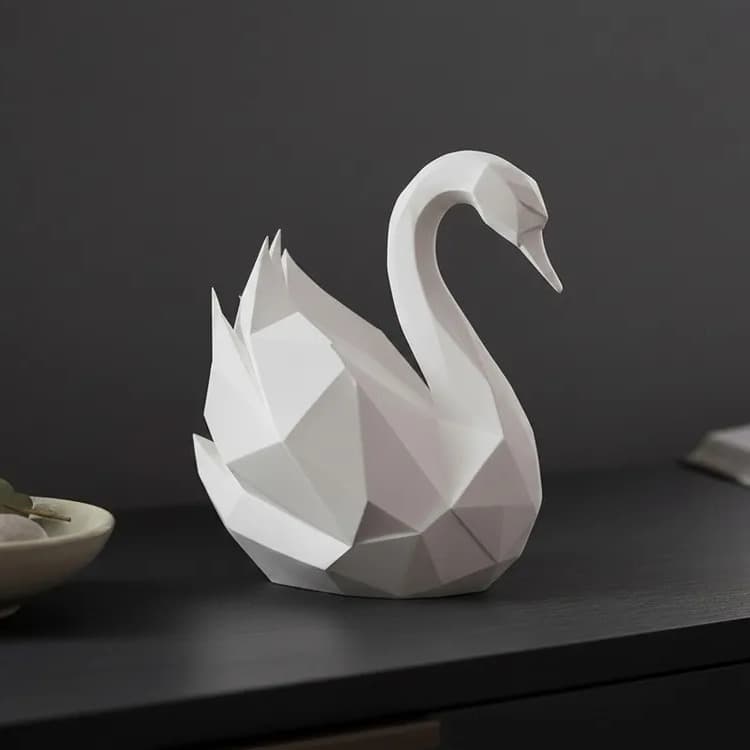 Svanefigur i low poly, mat elfenbenshvid, på en mørk skænk med en skål med sten og en bog