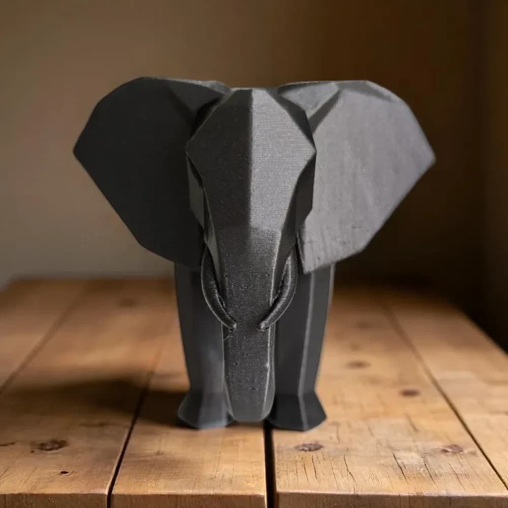 Sort elefantfigur i low poly set forfra med udspilede ører på et gammelt plankebord i varmt lys