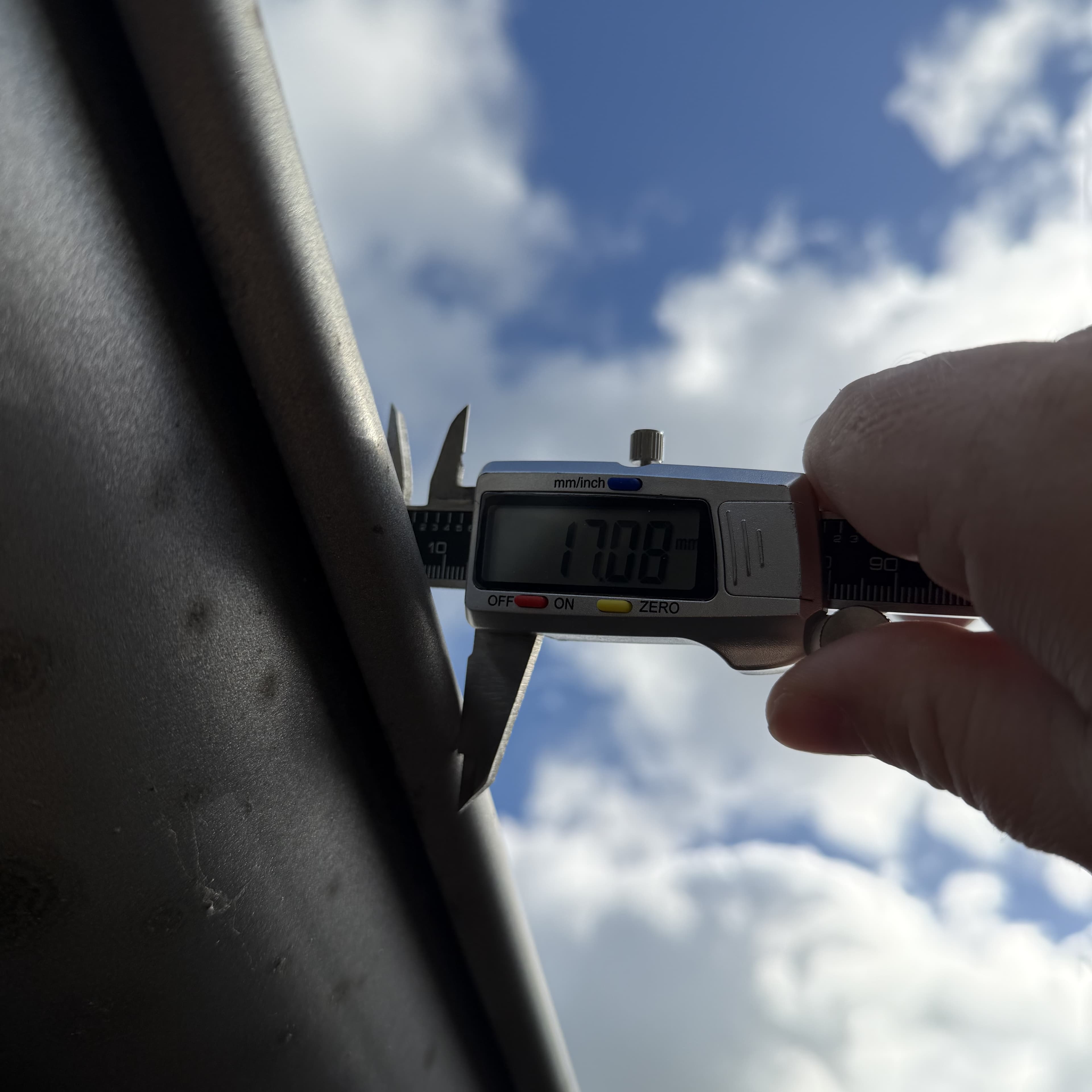 Den runde vulst på en tagrende måles med en digital skydelære mod blå himmel