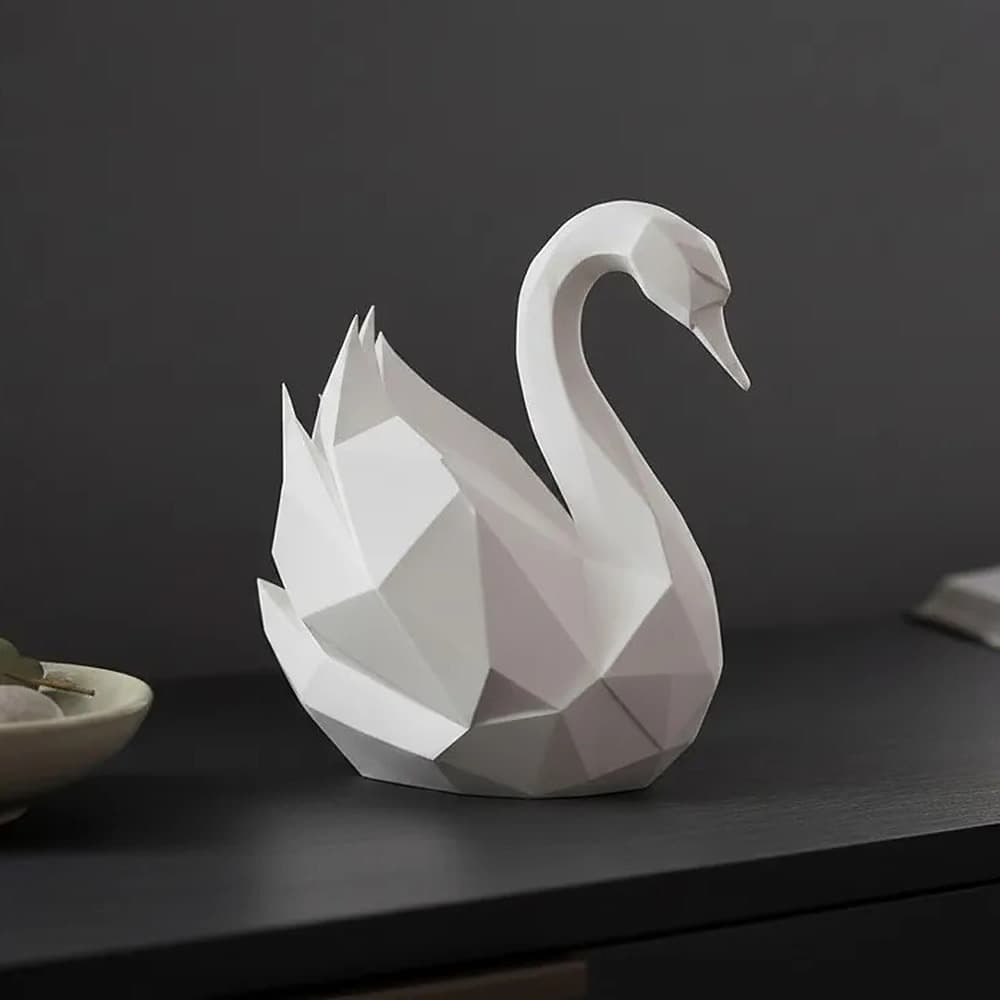 Svanefigur i low poly, mat elfenbenshvid, på en mørk skænk med en skål med sten og en bog